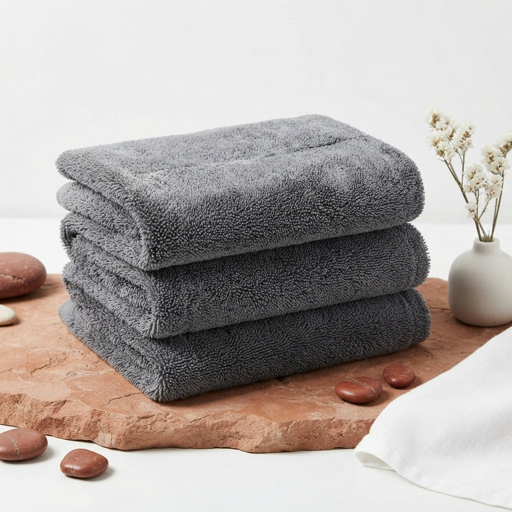 A grey twisted microfiber car towel neatly folded on a terracotta-colored surface in a professional studio setting.